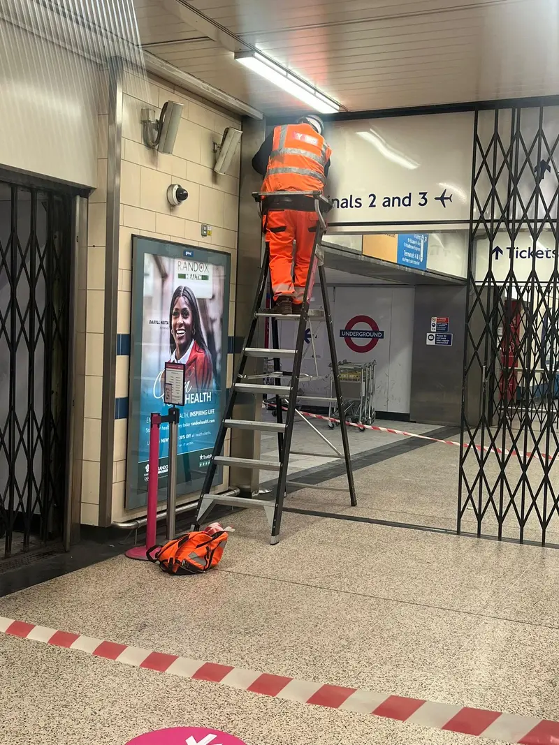 Engineers fitting collapsible grilles beneath a Terminals 2 and 3 sign